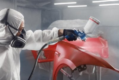 Car painter sprays red color paint to part of vehicle